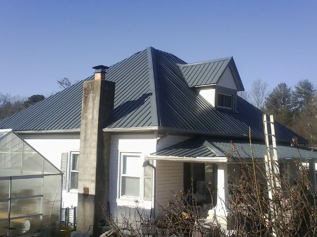 Dark blue standing seam metal roof on a white farmhouse with dormer — Slate & Tile Roof Repair by Roofing Brothers in Blanco