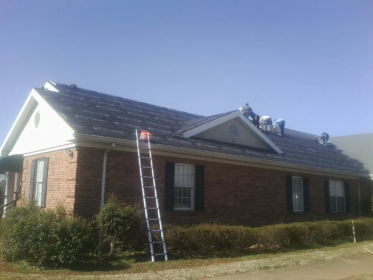 Crew tearing shingles off a brick ranch roof with a ladder set — Emergency Roof Repair work by our crew in Blanco