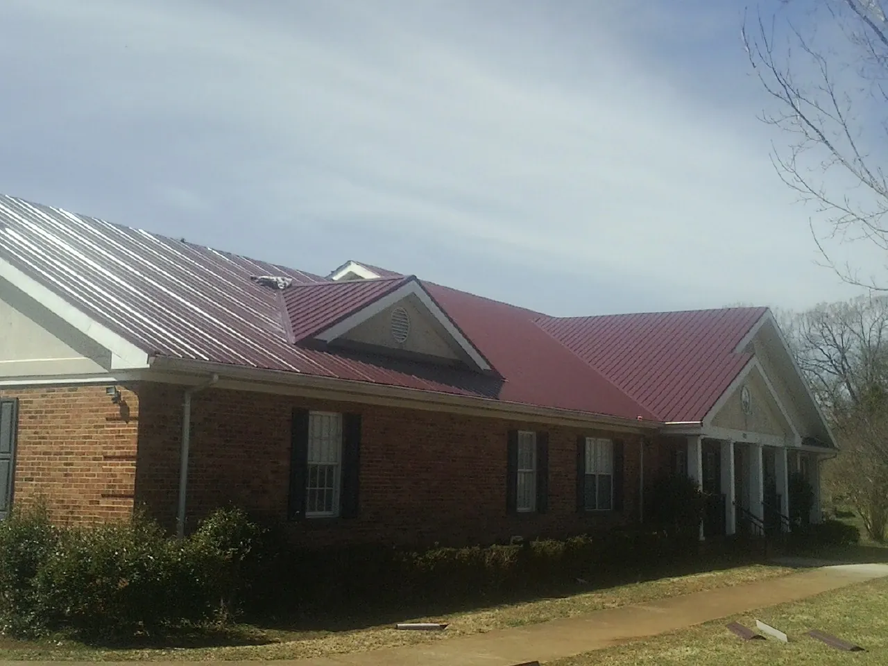 Red metal roof with gabled entries on a long brick building, from a Hail Damage Roof Repair job in Blanco