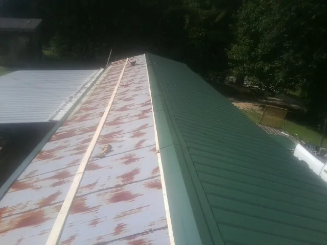 Old rusted panels beside newly installed green metal roofing — Wind Damage Roof Repair by Roofing Brothers in Blanco