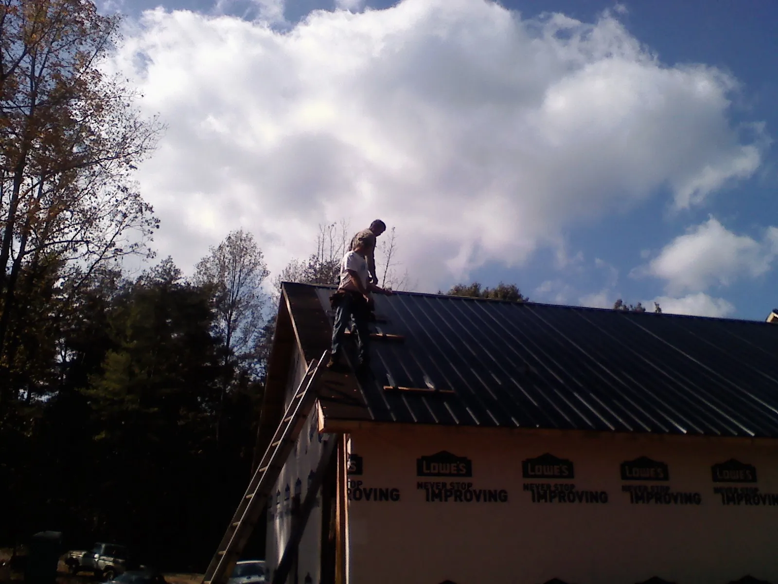 Roofer fastening dark metal panels high against a cloudy sky, from a Roof Inspection job in Blanco